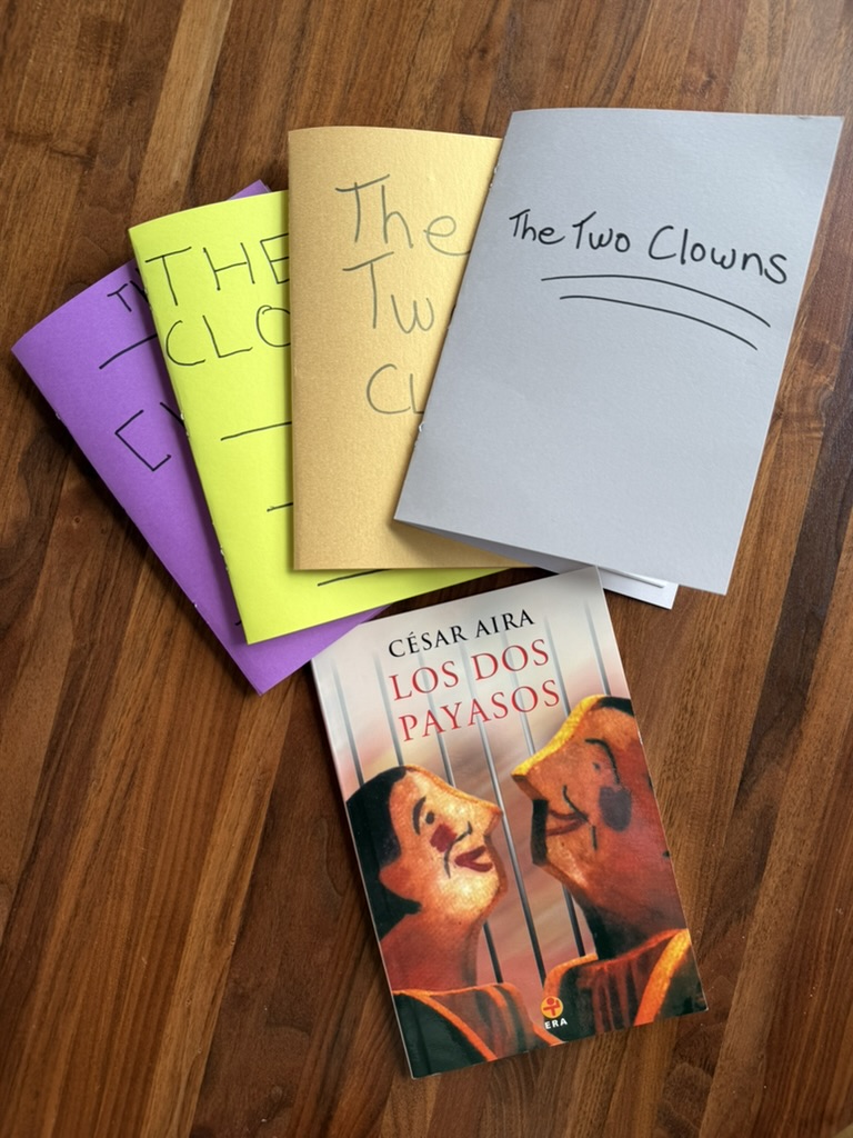 Photo of Cesar Aira's Los Dos Payasos beside several printed English draft booklets titled The Two Clowns on a wooden floor.